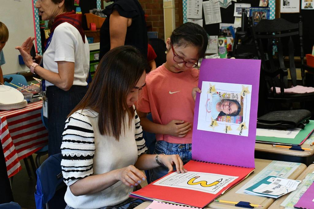 adult and child reading a book that the student made while sitting at her desk