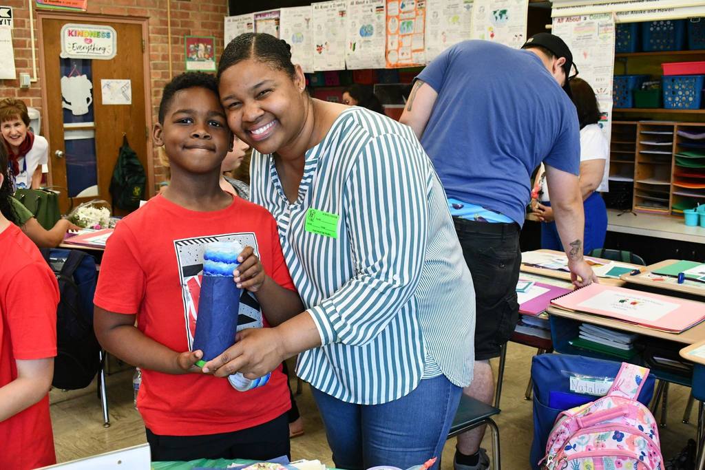 adult and student holding a craft while smiling together