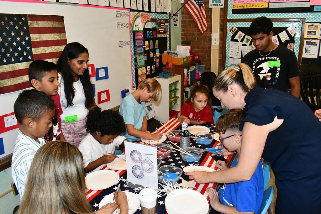 a bunch of students sitting around a table making crafts with an adult assisting