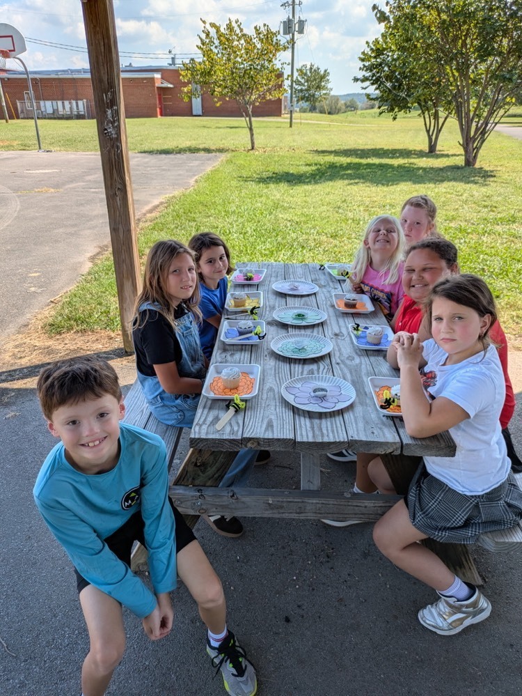 students sitting at picnic table with cupcakes and sprinkles