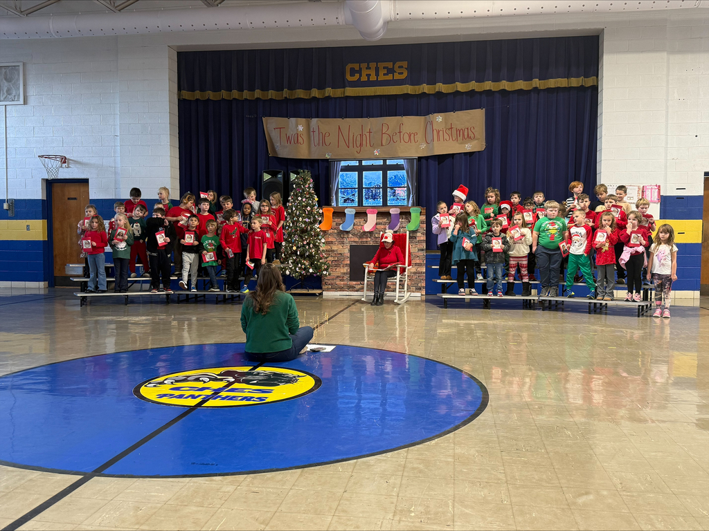 Mrs. Williams sitting facing students while students stand on risers facing out toward the crowd during the Christmas program. 