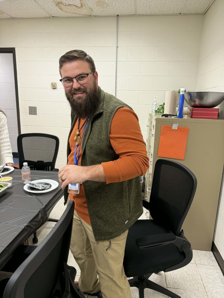 A man with a beard and glasses stands at a table with a plate and water bottle.