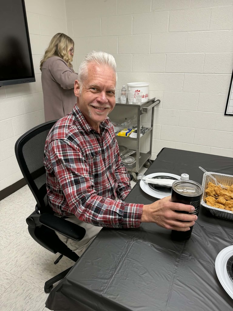 Man in a plaid shirt sitting at a table, smiling. 
