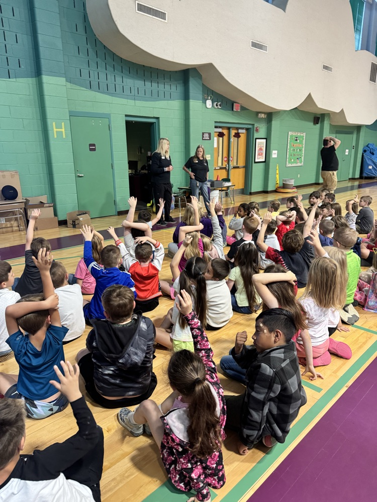 students raising their hands while sitting on the floor