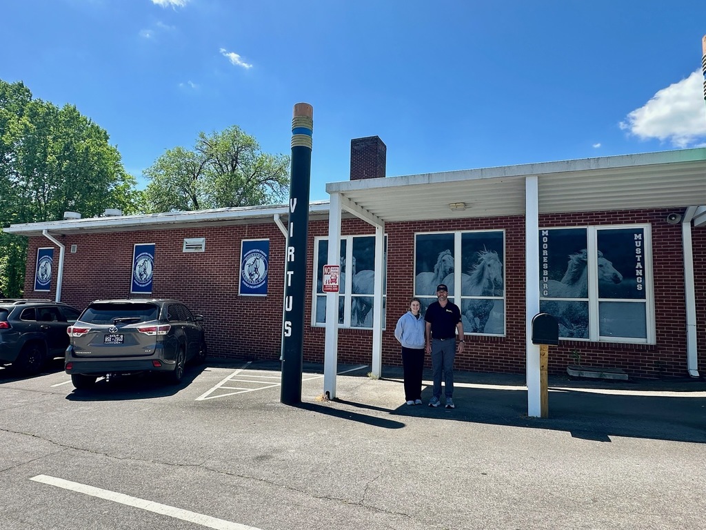 Two people stand in front of a red brick building with glass windows with new window films featuring the name of the school Mooresburg Elementary.