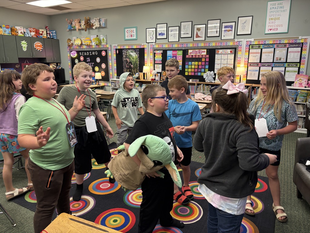A group of children in a classroom engage in an activity with a stuffed toy while standing on a colorful rug.