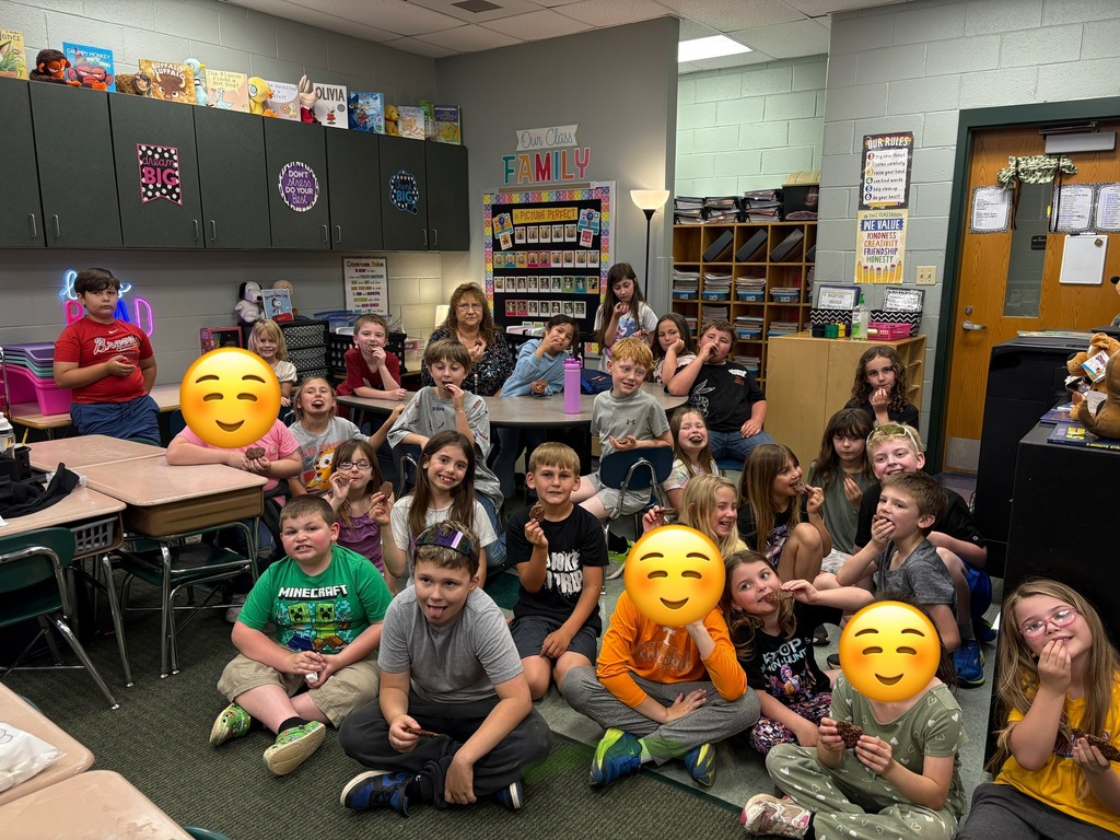 Children in a classroom pose with emoji masks. They sit on the floor and around desks.