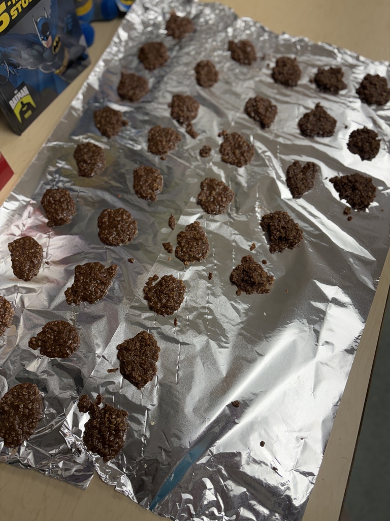 Chocolate cookies arranged on silver foil, with a Batman bag in the background.