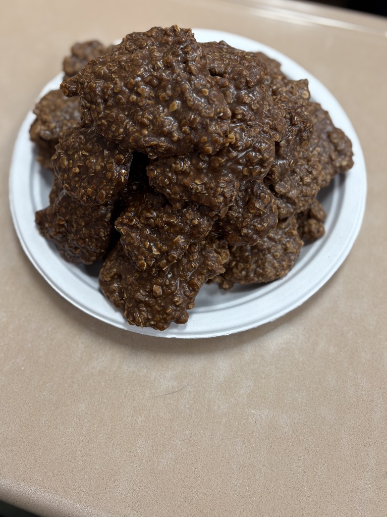 A white plate holds a stack of round chocolate cookies with a crumbly texture. The cookies rest on a light beige surface.