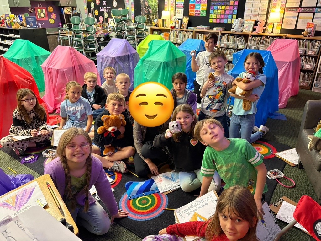 A group of children are sitting and kneeling on the floor, surrounded by colorful tents.