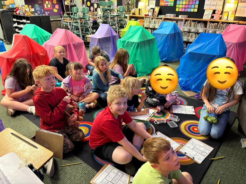 Children sit on a rug, engaged in activities, in a colorful classroom with multicolored tents in the background.