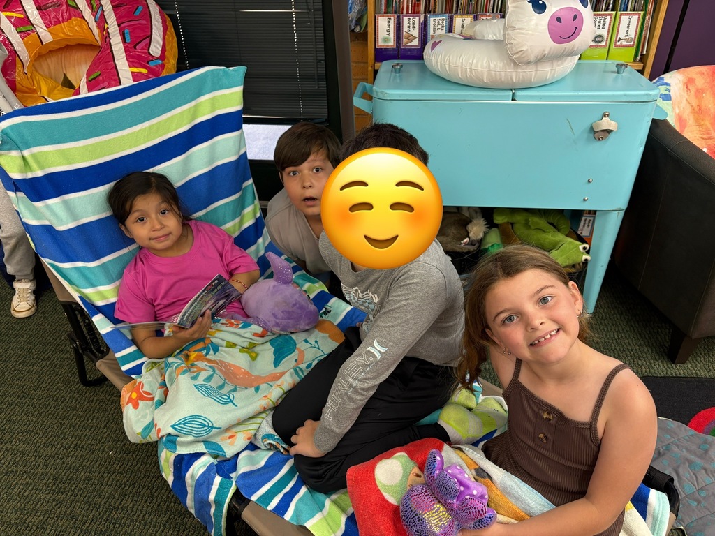 Four children in a classroom. Two girls and two boys. One wearing a mask, the others smiling.