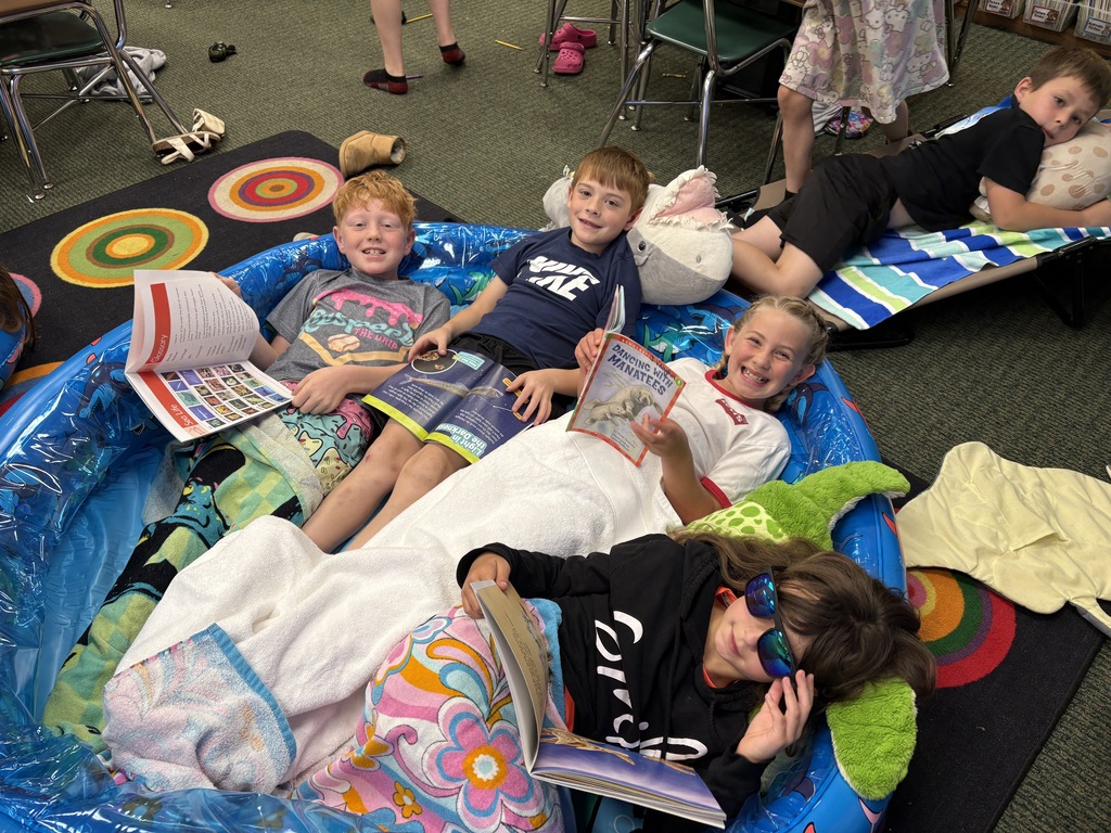 Five children, four boys and a girl, sit in a pool, reading books. Some wear sunglasses.