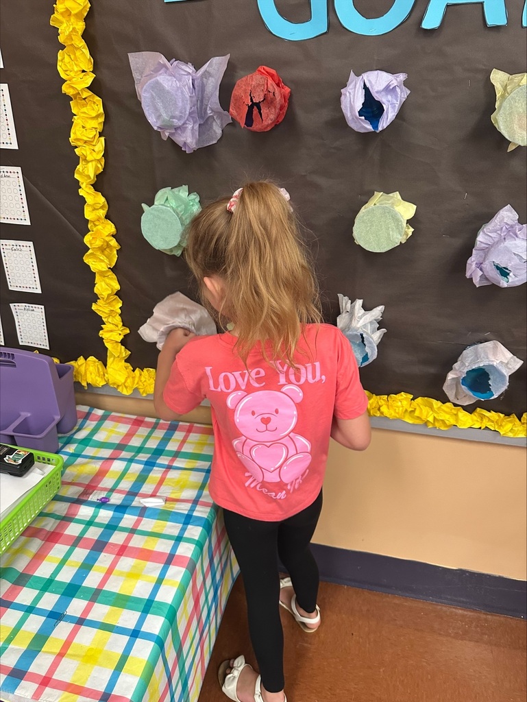 A child in a red shirt with a bear and "Love You" text touches colorful papers attached to a bulletin board.