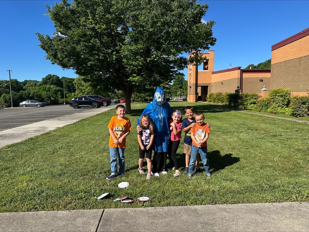 A group of children and a person in a blue costume pose for a picture on a lawn.