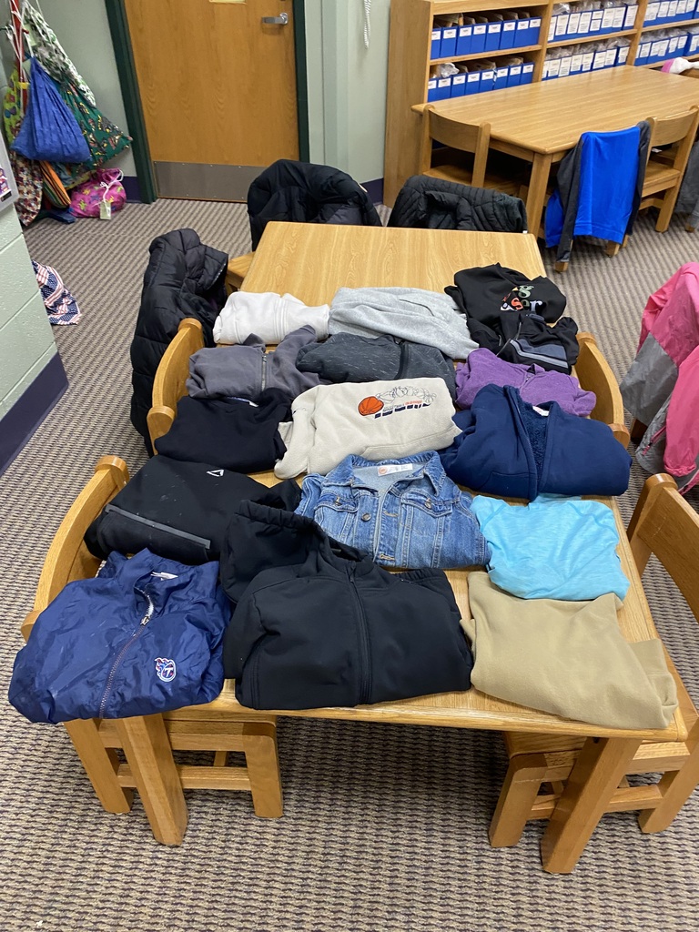 A table with jackets, shirts, and pants. Chairs and a door in the background.