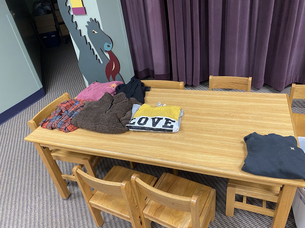A wooden table with several chairs around it holds assorted clothing, including a white t-shirt with "LOVE" in black letters.
