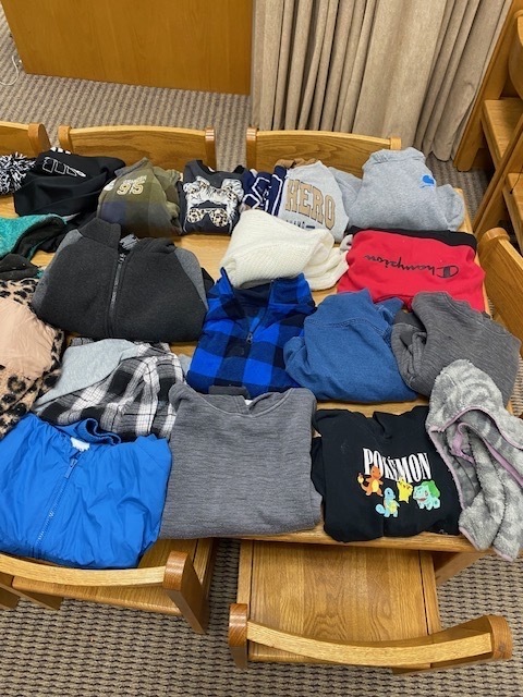 A table has various folded clothing items, including shirts, hoodies, and sweaters, of different colors and patterns.