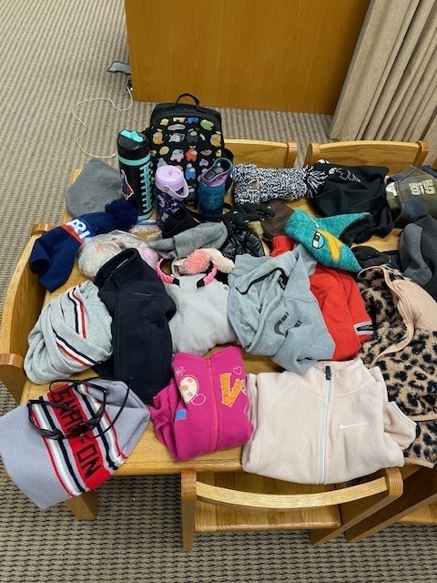 A table with various items including backpacks, a bottle, a hat, a blanket, a shoe, and a jacket.