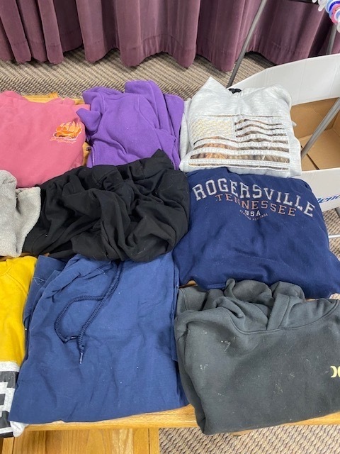 A table displays a variety of colored shirts, including purple, pink, black, and blue, on a beige floor.