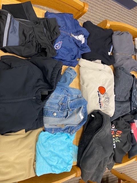 A collection of various jackets, jeans, and shirts neatly organized on a wooden surface. Background is blurred.