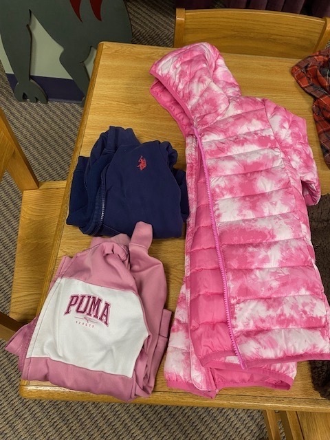 A wooden table with three jackets. One is pink tie-dye, another is pink with a white PUMA logo, and the third is dark blue.