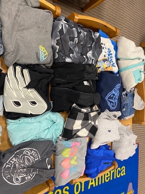 A wooden shelf displays various clothing items like hoodies, t-shirts, and socks, with one shirt featuring a 'NB' logo.
