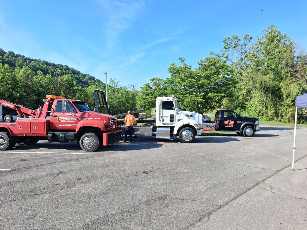 Three tow trucks parked in a parking lot with trees and a mountain in the background.