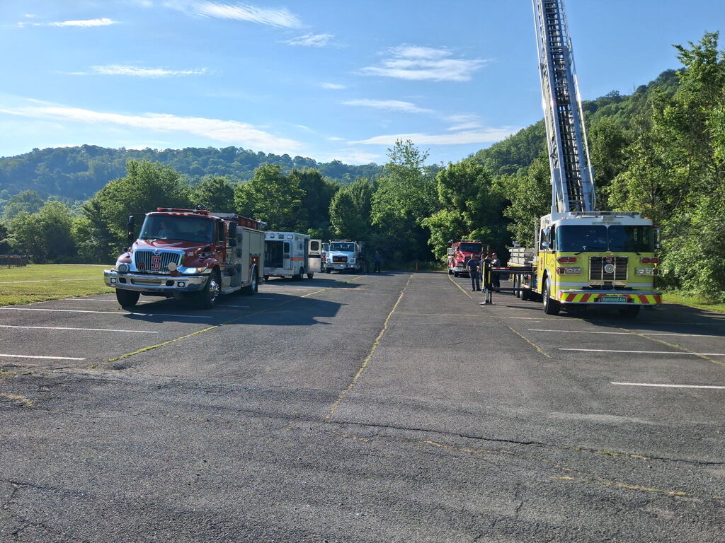 Fire trucks parked on a road with an extended ladder on one of the trucks. Trees and mountains are in the background.