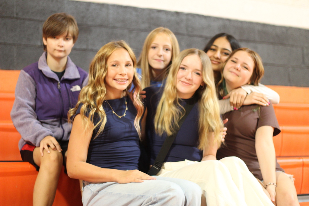 A group of seven people sit together on a bleacher. They are all smiling and appear to be posing for a picture.