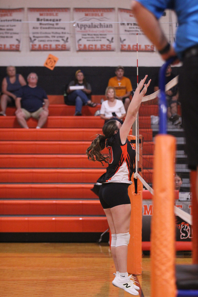 A player in black and white jersey reaching up with a volleyball net in front.