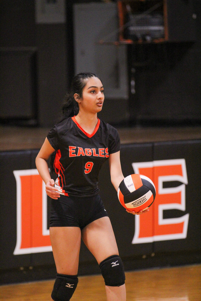 A woman on a court wearing a black jersey with the number 9, holding a volleyball.