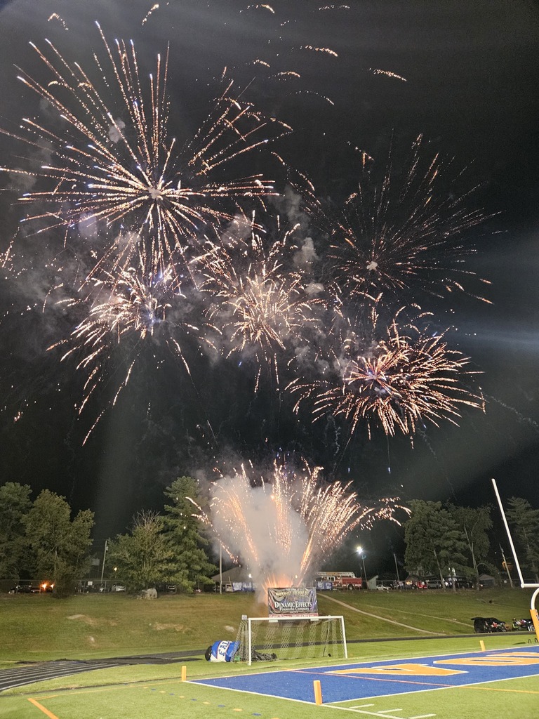Fireworks in a night sky above a field, with one in the air and others exploding.