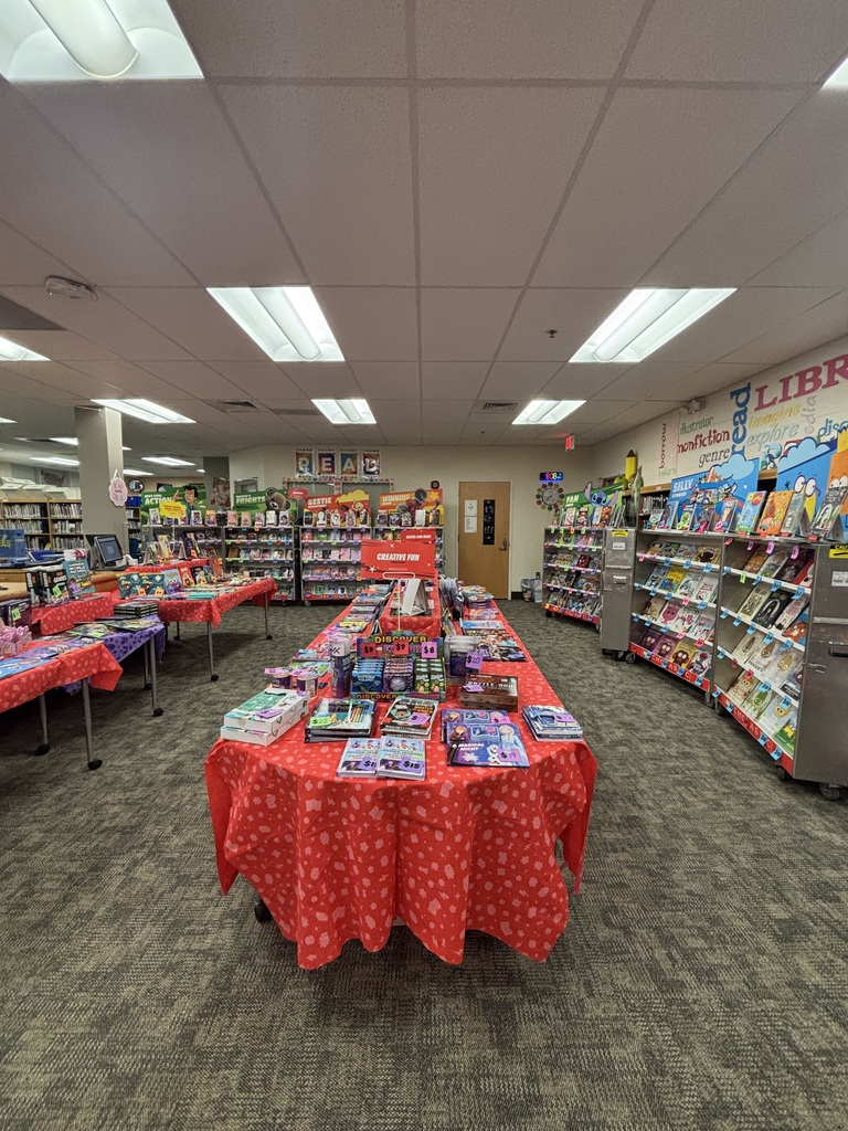 An indoor space resembling a bookstore with multiple tables, tables covered in red cloth, and books on display.