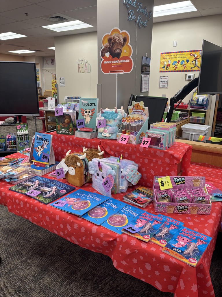 A red table covered in books, toys, and other items in a room with a television.