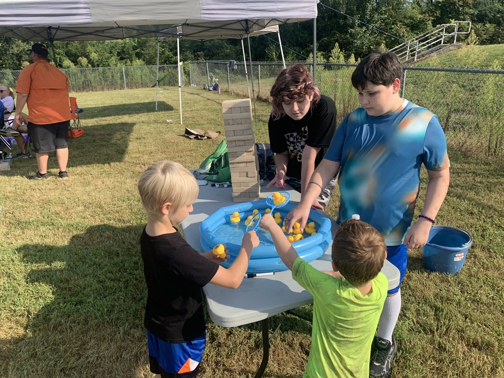Three children participate in a duck pond game, with a blue table and tent in the background.