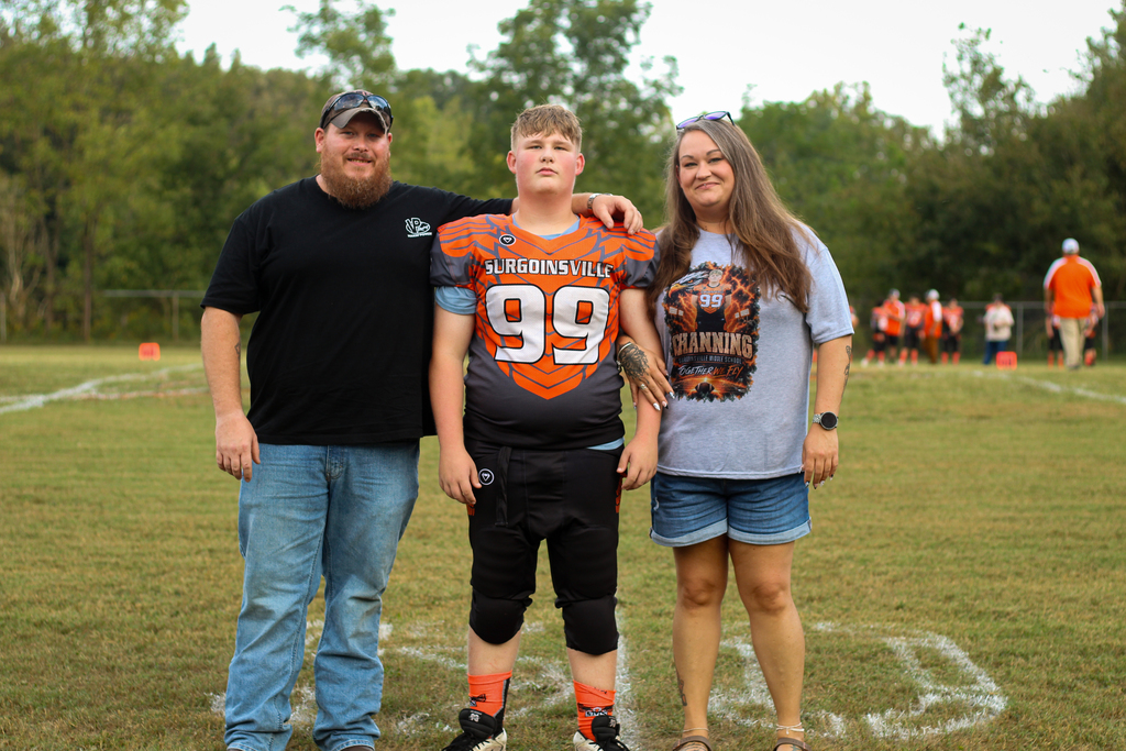 Three people on a football field, one wearing a jersey with number 99, another in a black shirt, and the third in a gray shirt.