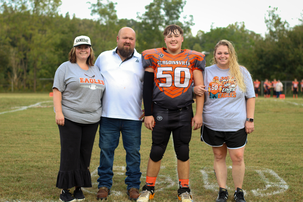 Four people in a football field. A young man in jersey number 50 stands between two women and a man.