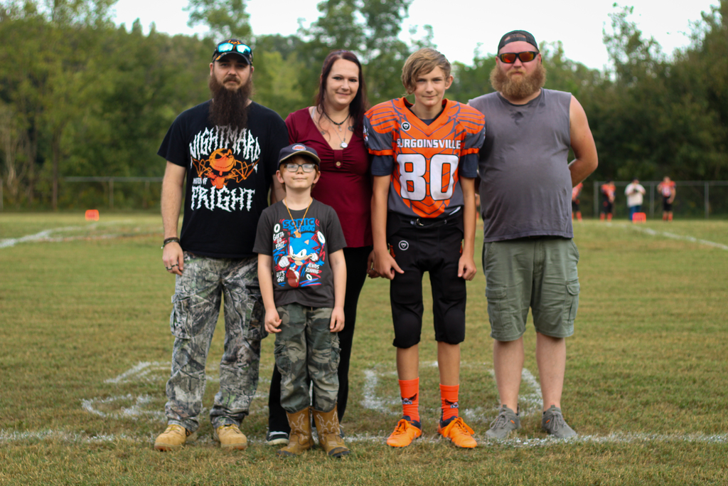 Five people on a football field, two adults and three children. A boy in a football jersey.