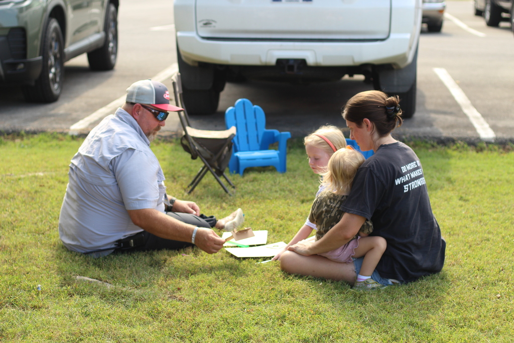 Man and woman sitting on grass with two young children. A table with papers and pens.