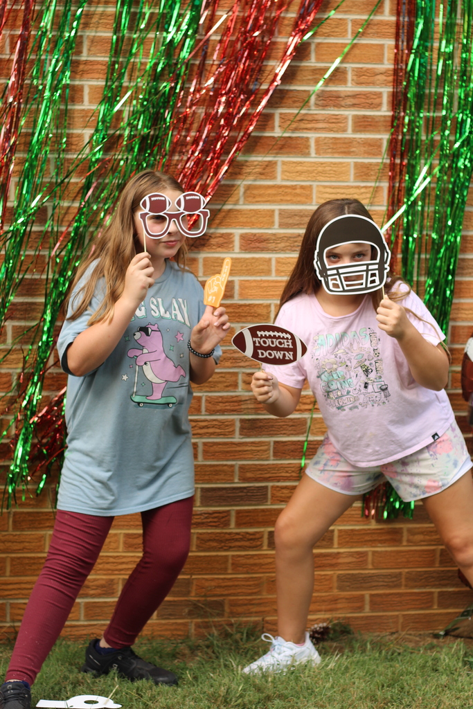 Two girls pose in front of a brick wall with red and green streamers. One wears a football helmet.