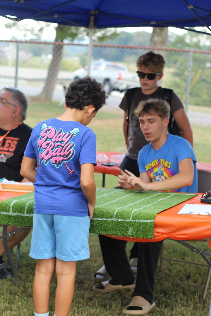 Four people sit at a table with a football-themed tablecloth. Three wear blue shirts, and one wears black.