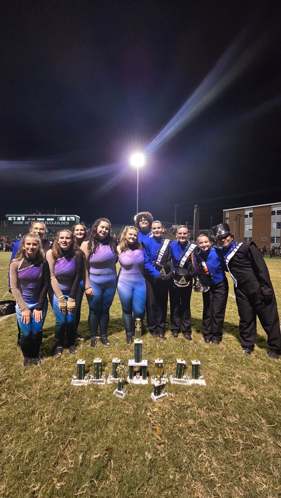 Group of students pose for photo with trophies on a grassy field at night.