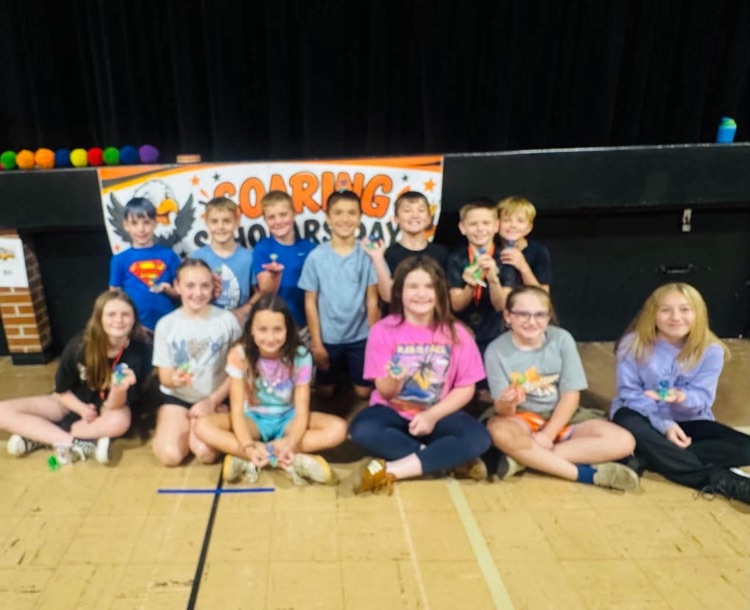 Group of students sitting in a semi-circle, posing for a photo in a gym. Banner in background.