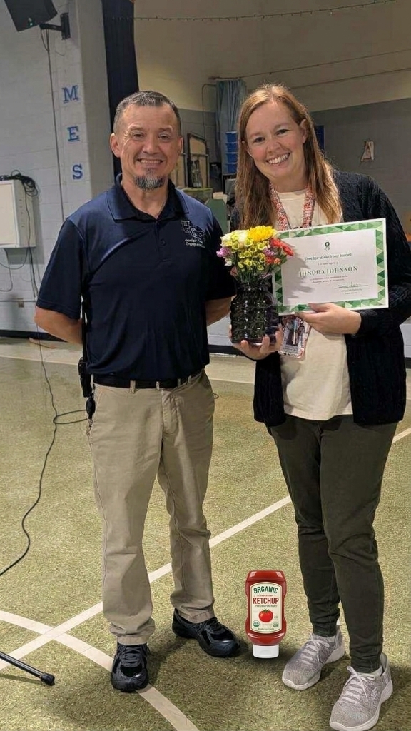 A man and woman stand next to each other, holding a vase of flowers and a certificate.