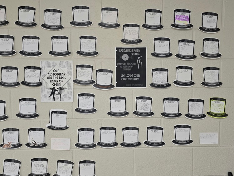 A bulletin board with many black top hats with papers and a poster about recycling.