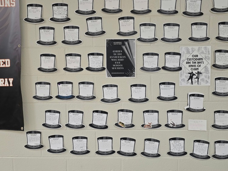 A wall with many black hats, a banner, and a poster with a drawing of people.