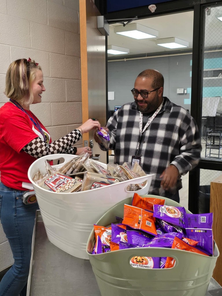 Two people standing at a table with two large containers of food, one person handing food to another.
