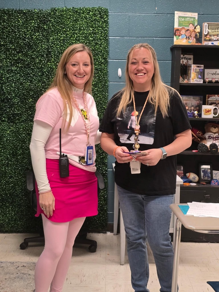 Two women standing next to each other in a room with a green wall and a bookshelf.