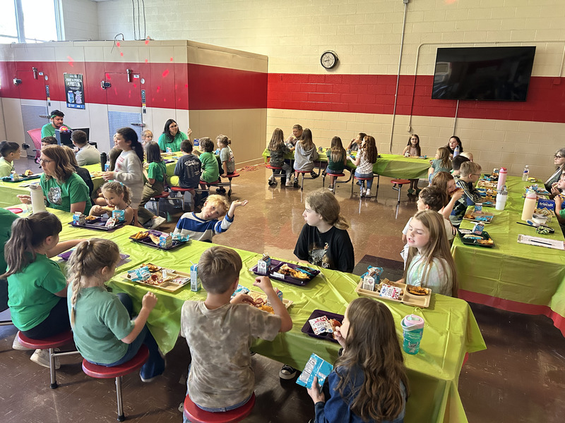 Students eating lunch in school cafeteria with green table cloths.